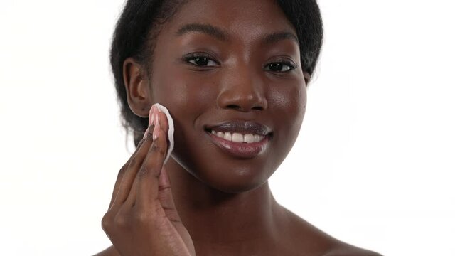 Close up of an african woman taking off her makeup from her face using a cotton pad. Showing the cotton pad to the camera. White background.