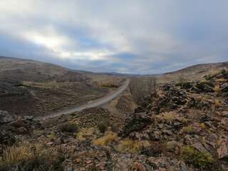 The empty asphalt highway across the golden field and hills at sunrise. 