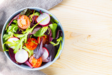 Healthy salad with cherry tomatoes, radish and mix salad. Salad with mix of greens on wooden background. Copy space