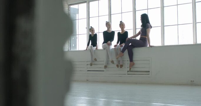 Teen girls talking to their coach after a dance class. Young dancers sitting on windowsill, chatting and laughing 4k footage