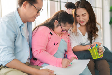 Happy asian family sitting on sofa and  together paint with their daughter down syndrome child in living room at morning time, Activity happy family lifestyle concept,