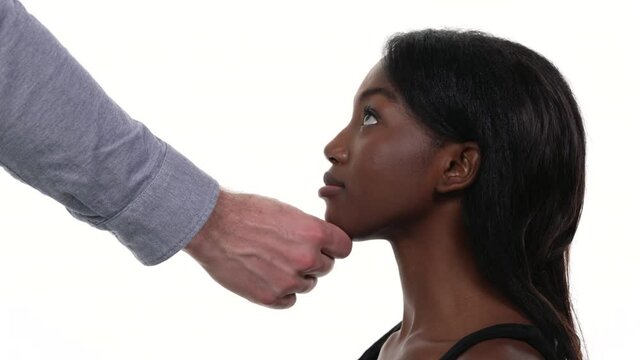 Closeup of African woman holding her head down and a caucasian male hand touching the chin and raising it up. Physical harassment in workplace
