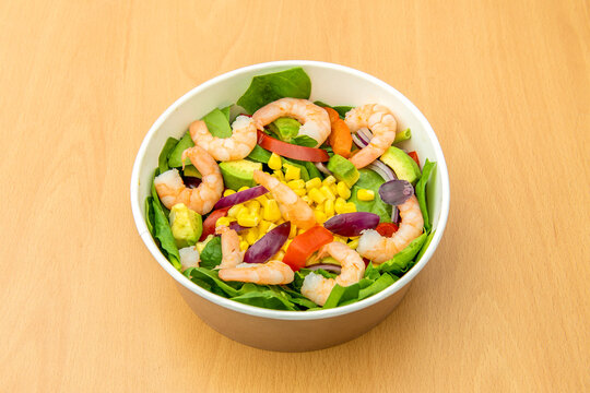 home delivery bowl with a salad of green spinach, yellow sweet corn, pink cooked shrimp, raw red bell peppers and diced red onion