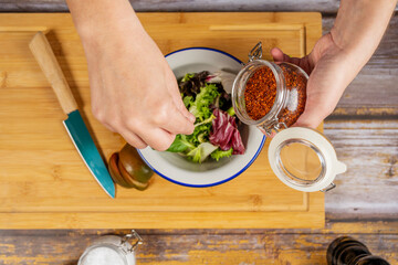 woman's hands seasoning mixed lettuce sprout salad. Put paprika in the tomatoes.