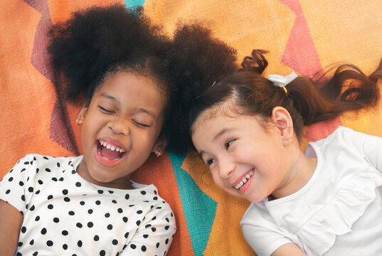 Happy cheerful ethnic girls  laying on mat at outdoors park, Her smiling and laughing together, Relationship little kids, Diverse ethnic concept.