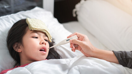 Obraz na płótnie Canvas Asian mother measuring temperature girl with digital thermometer in her mouth on bed at morning time, Sick child have cool towel for reduce high fever, Selective focus, Healthy and infection concept