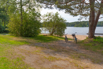 Two bicycles parked in the shadow by a sunny beach.