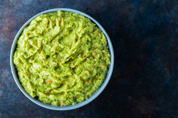 Guacamole in a gray bowl on a dark background. Bowl of avocado guacamole sauce with fresh ingredients. Copy space. Top view