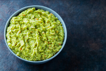 Guacamole in a gray bowl on a dark background. Bowl of avocado guacamole sauce with fresh ingredients. Copy space. Top view