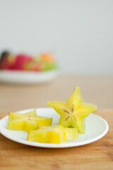 Exotic starfruit or averrhoa carambola on white plate on wooden cut board. Healthy food, fresh organic star apple fruit.