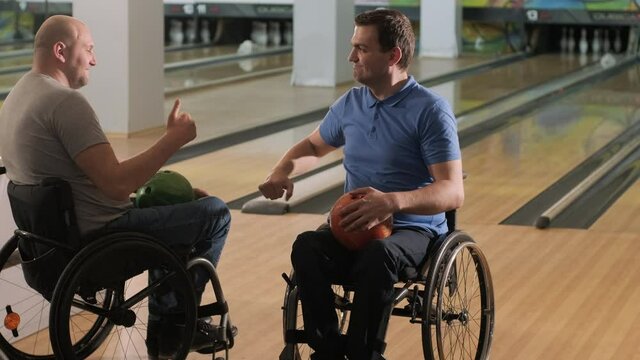 Two young disabled men in wheelchairs playing bowling in the club