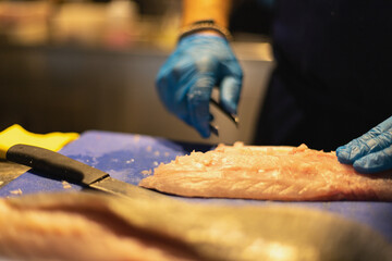 the chef cuts the fish in blue gloves