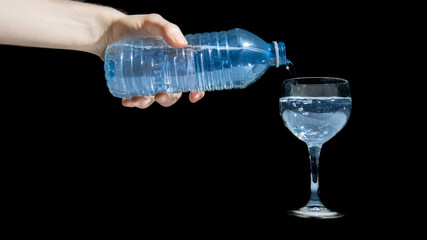 Pouring a glass of water from water bottle refreshing drink isolated black background. Filling glass with sparkling blue water