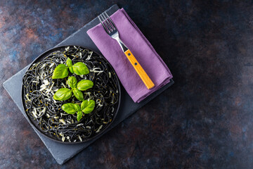 Pasta spaghetti with parmesan cheese, basil and pesto sauce. Black pasta with cuttlefish ink on a dark background. Vegetarian pasta with basil pesto. Top view. Copy space