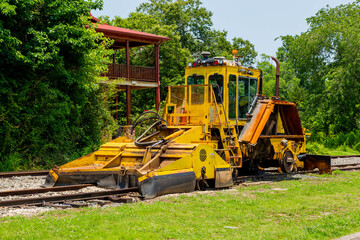 Fototapeta na wymiar Large Yellow Train Car Tractor on a Rail Road with Trees and Property in the Background