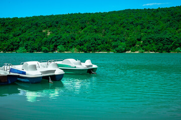Row of white catamaran stands on the lake. Catamaran near the pier in sunny weather against the backdrop of green hills.