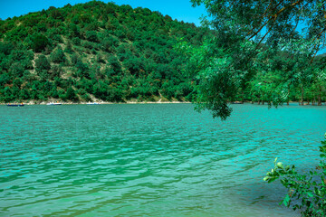 Beautiful lake with turquoise water surrounded by green hills. The lake with small boats is surrounded by mountains with a forest.