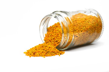 bee pollen in a transparent glass jar spilled on a white background