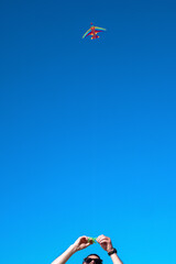 man holds a rainbow color kite flying high in the blue sky in summer. young guy launches a kite in summer in hot weather