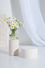Empty cylindrical cor plinth with chamomile flowers on a white background. Blank shelf product...