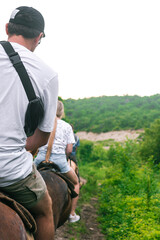 A young guy in a white T-shirt walks on a horse through the woods. A rider on a horse is walking through a large and dense green forest.