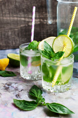 Glasses of basil lemonade with mint, lime, lemon and ice on light gray background