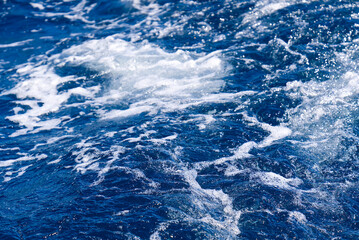 Obraz na płótnie Canvas Abstract blue sea water with white wave for background. Adreatic sea, blue mediterranean sea. sea splash sailing boat trail on the water
