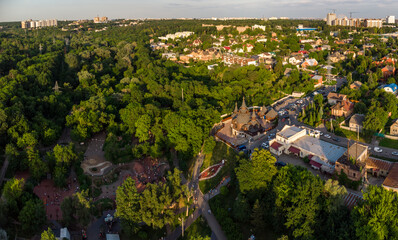 Aerial evening view on playground and church in green summer Kharkiv city center popular recreation park Sarzhyn Yar. Botanical garden in residential area in sunset light