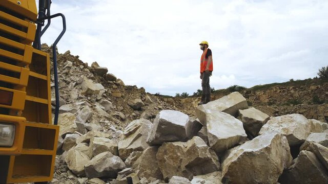 Male employee giving commands to excavator on quarry