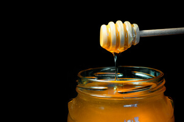 honey flows on a wooden spoon in a jar on a black background. High quality photo