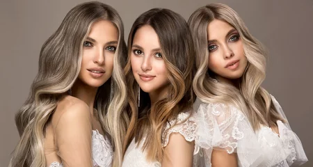 Rolgordijnen Three beautiful girls in  white wedding dresses  with hair coloring in ultra blond. Stylish hairstyle curls done in a beauty salon. Fashion, cosmetics and makeup.Adorable brides © Sofia Zhuravetc