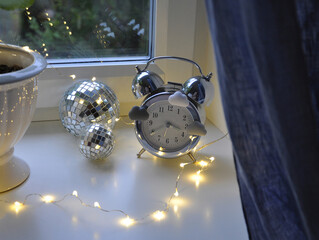 silver retro clock and LED garland behind the curtain by the window