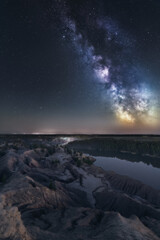 Milky Way galaxy, mountains and lake at clear sky in Romantsevskiye Gory, Konduki at starry night. Astrophotography of nature landscape