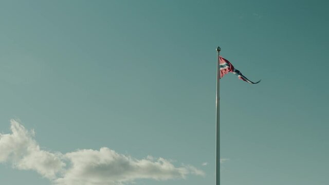 Norwegian pennant flag moving in strong wind with a beautful turquoise sky and a peaceful cloud in Norway, slow motion