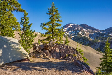 Back country campsite with small tent and a view of pumice covered moraine, fir trees on a cliff,...