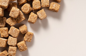 Brown cane sugar cubes placed on a beige background. View from directly above.