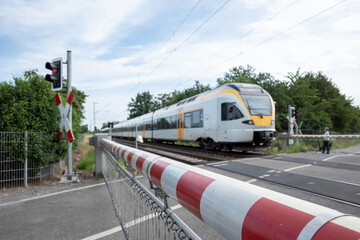 Selective focus view at red and white level crossing railway barrier which block the road and regional train move on the rail on countryside in Germany.	 - obrazy, fototapety, plakaty