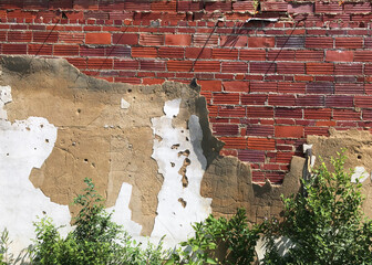 Weathered cement plaster peeling back to expose old red brick wall of abandoned building in American Midwest.