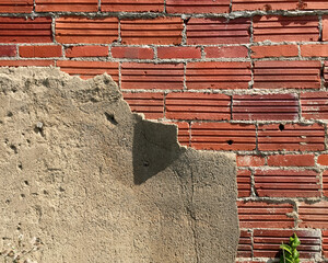 Weathered cement plaster peeling back to expose old red brick wall of abandoned building in American Midwest.