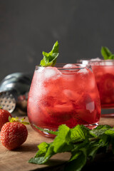 Red drink with strawberry, ice and mint. Refreshing summer cocktail in a glass on wooden table