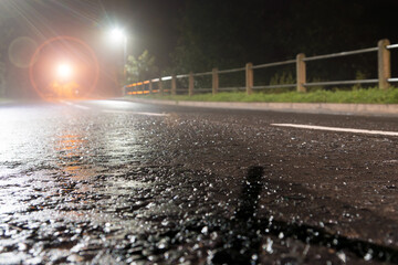 A low angle, shallow depth of field of tarmac highlighted by street lights. On a rainy country road at night.