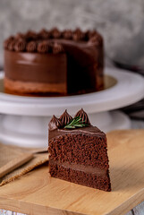 Slice of delicious homemade chocolate cake soft fudge topping with rosemary on wooden board.