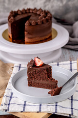 Slice of delicious homemade chocolate cake soft fudge topping with strawberry on white plate.