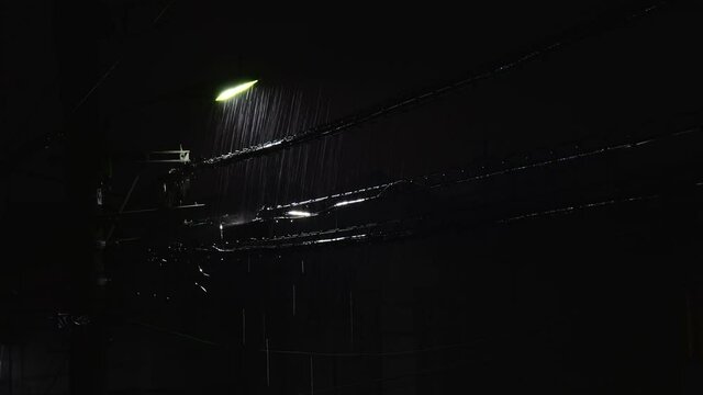 電柱に付けられた街灯に照らされる激しい雨と電線から滴る水滴