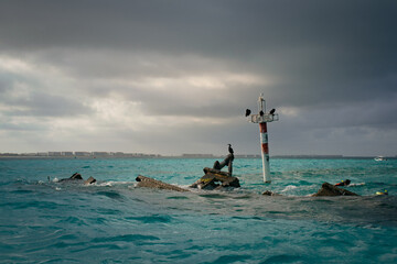 An almost completely sunken boat and lighthouse in ocean.