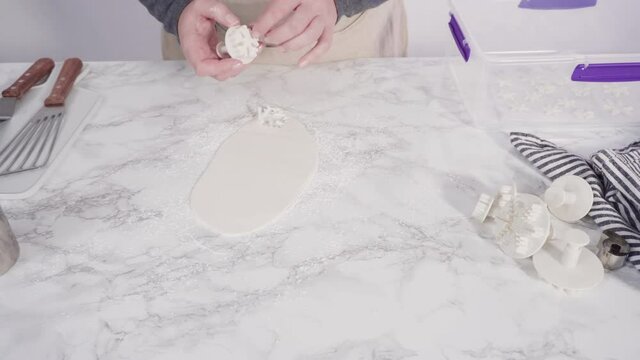 Step by step. Cutting out snowflakes with cookie cutters out of white fondant on a marble counter.