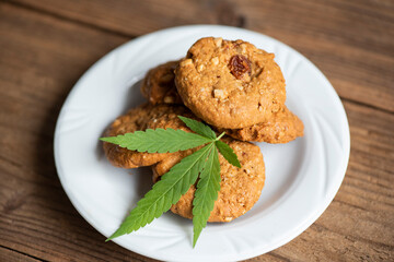 Chocolate cookies with cannabis leaf - marijuana leaves plant on white plate on the wooden table nature herb, cannabis food concept