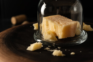sliced parmesan cheese with chipped pieces, covered with a glass jar, on a dark background