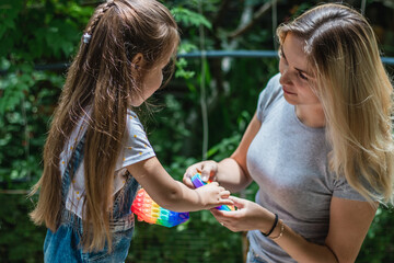 Naklejka premium A child and his mother playing with a pop-fidget on a green background. A girl and a mother click on a colored rainbow silicone anti-stress toy Push pop bubble. Communication with children.