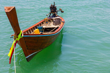 Obraz premium Traditional longtail wooden boat with colorful stripes on its nose parking over clean and clear sea water at a local pier waiting for tourists